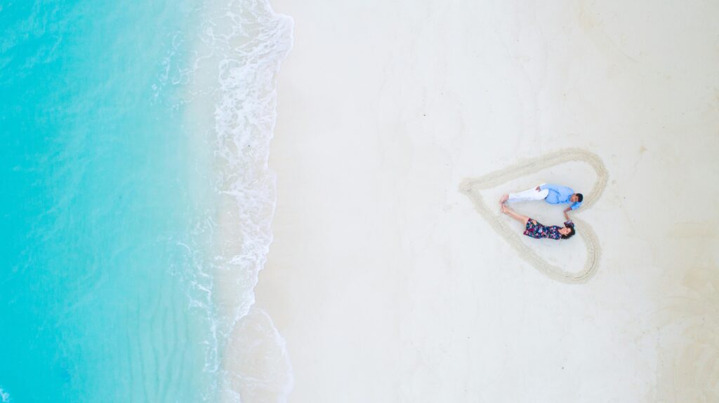 Aerial view of a couple lying on a beach in the Maldives, framed in a heart shape in the sand.
