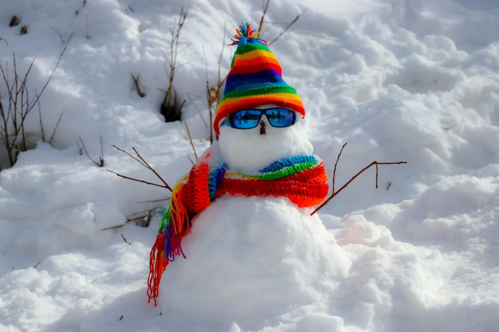 A vibrant snowman adorned with a rainbow scarf and hat in the snowy landscape of Manali, India.