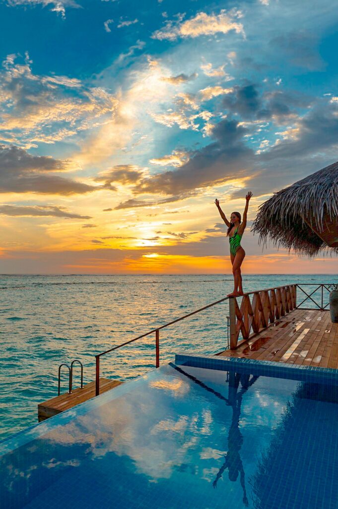 Woman enjoying a serene tropical sunset at a luxurious overwater bungalow resort.
