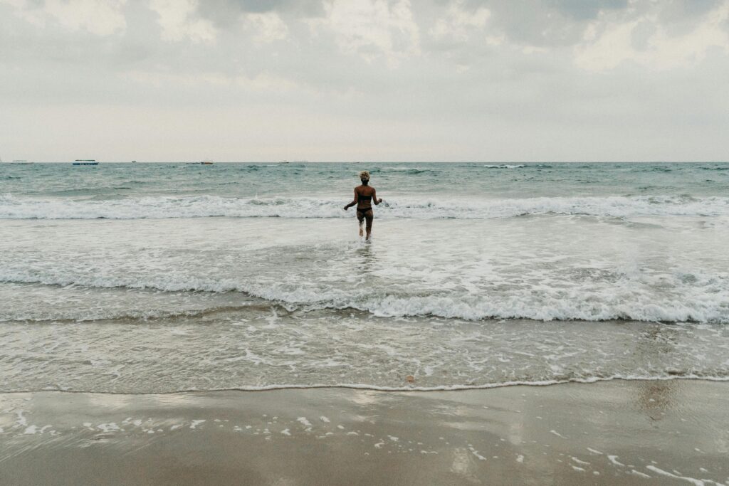 A young woman with curly hair wades into the ocean on a peaceful beach day.