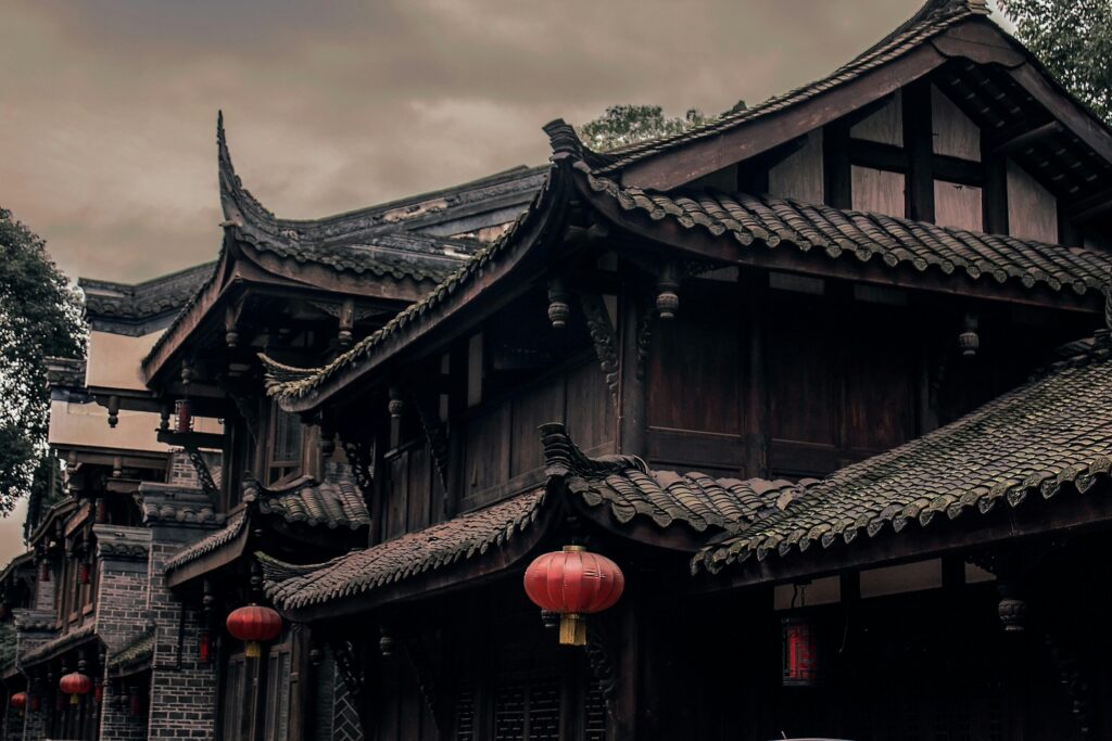 Historic Chinese building with ornate roofs and red lanterns under cloudy skies.